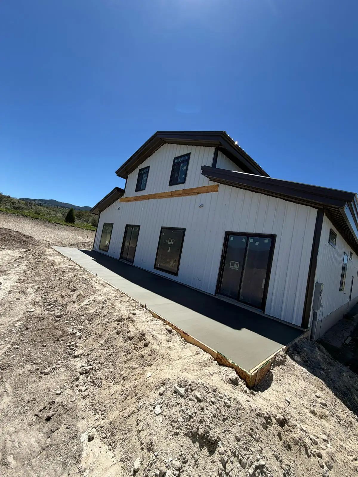 New concrete walkway wrapping a white metal barndominium on a hillside lot